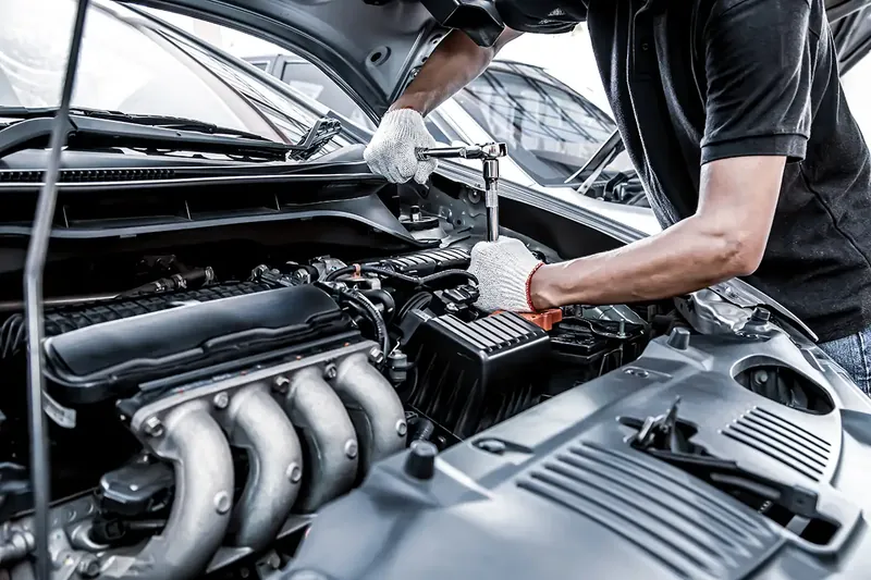 Mécanicien ganté travaillant sous le capot d’une voiture, moteur visible (photo d’illustration – entretien Fast Depann)