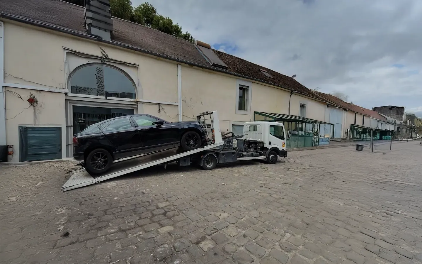 Plateau chargeant une BMW noire devant un bâtiment ancien, dans une cour pavée (photo d’illustration – à Cavaillon (84300))