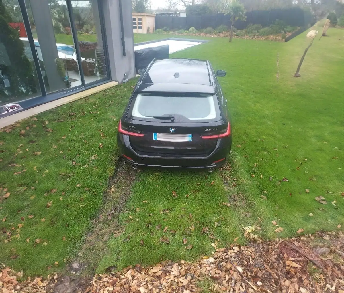BMW break noire enlisée sur une pelouse détrempée, ornière creusée derrière la roue arrière